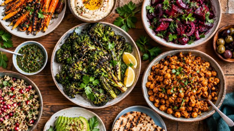Colourful vegan sharing plates of curries, grilled vegetables and flatbreads on a wooden table