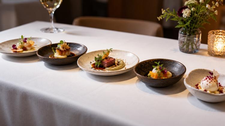A row of small tasting-menu courses on fine ceramic plates on a white tablecloth