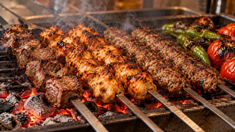 Lamb shish, chicken shish and kofte skewers cooking over glowing charcoal with peppers and tomatoes