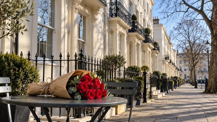 A bunch of red roses wrapped in brown paper on a cafe table outside a cream stucco Regency terrace
