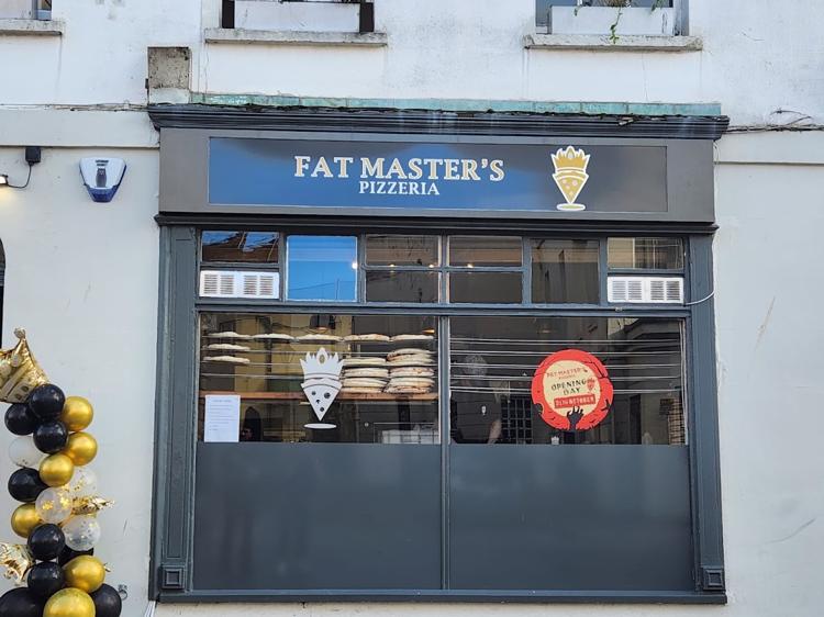 The navy shopfront of Fat Master's Pizzeria on Regent Street, Cheltenham, with pizza boxes stacked in the window