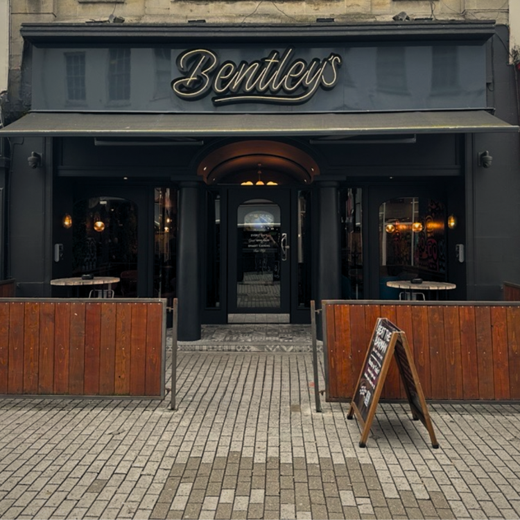 The dark front of Bentleys Bar on Cheltenham High Street, with tables behind wooden screens