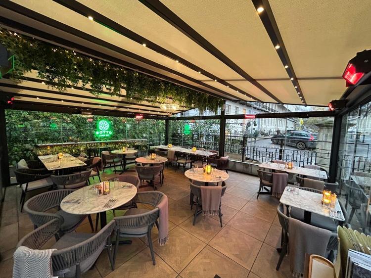 Marble tables and grey chairs under a slatted roof and trailing greenery in the glass conservatory at Sotto, Imperial Square, Cheltenham