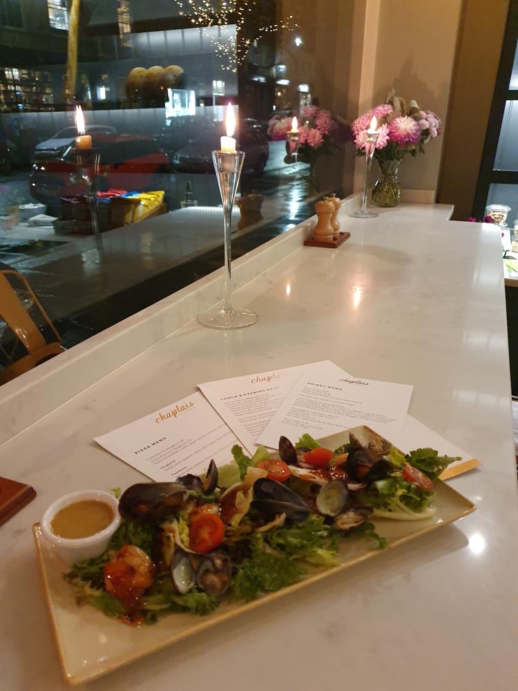 A plate of mussels and salad on a marble counter by candlelight at Chaplais Kitchen, Cheltenham