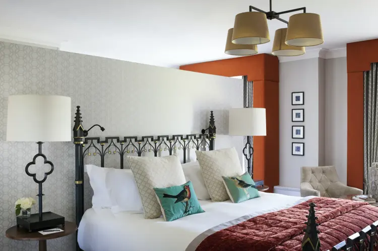 A bedroom at the Queens Hotel, Cheltenham, with a dark iron bed, white linen and an orange feature wall