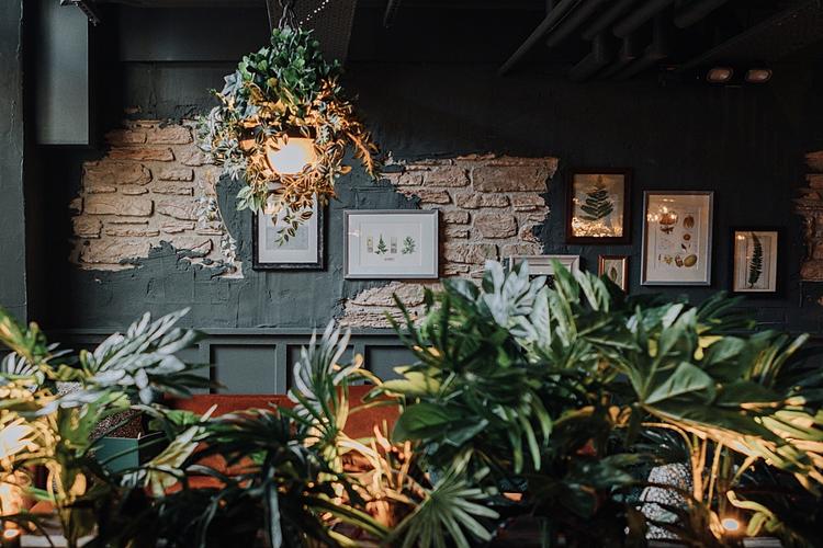 Plants and framed pictures against a dark wall inside The Botanist, Cheltenham