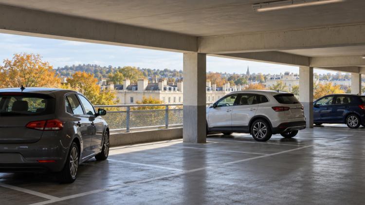 Cars parked on an upper deck of a multi-storey car park with cream Regency rooftops and autumn trees beyond, in Cheltenham