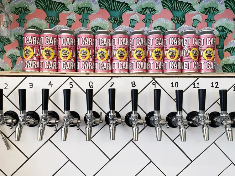 A row of numbered beer taps under stacked cans at Planet Caravan, Cheltenham